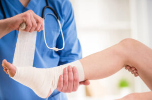 A closeup image of a doctor wrapping a patient's ankle and foot in a bandage.