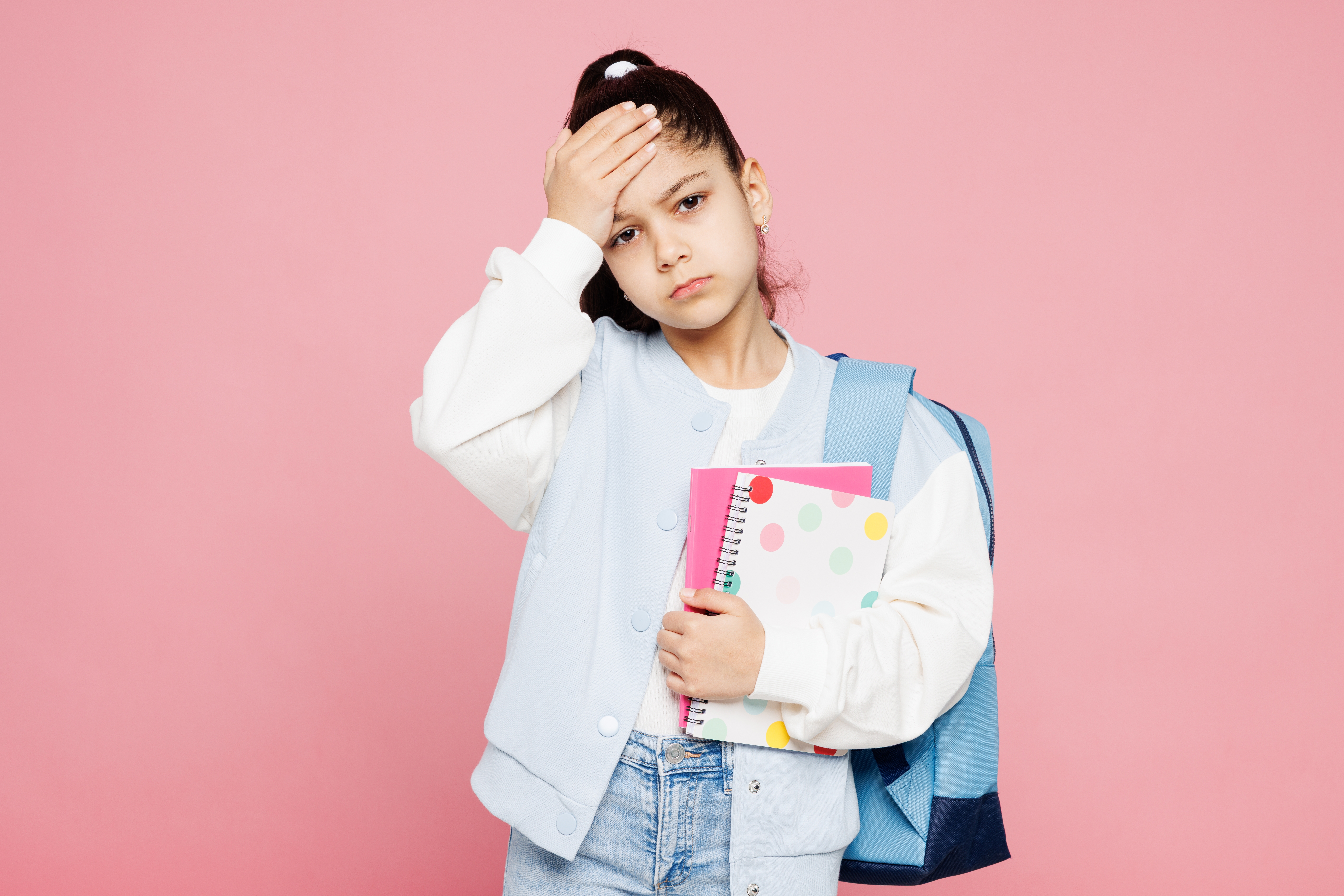 Young sick schoolgirl wearing backpack and holding her head in pain