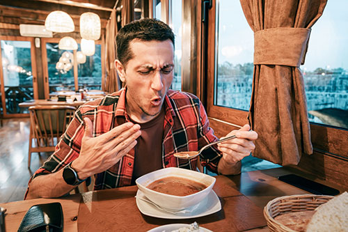 A man eating a bowl of hot soup recoils in pain