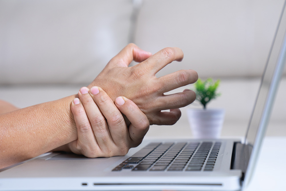 A person at their computer grabbing their wrist.